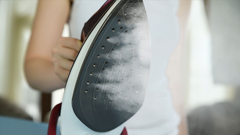 iemand heeft strijkijzer vast om te strijken waar stoom uit komt